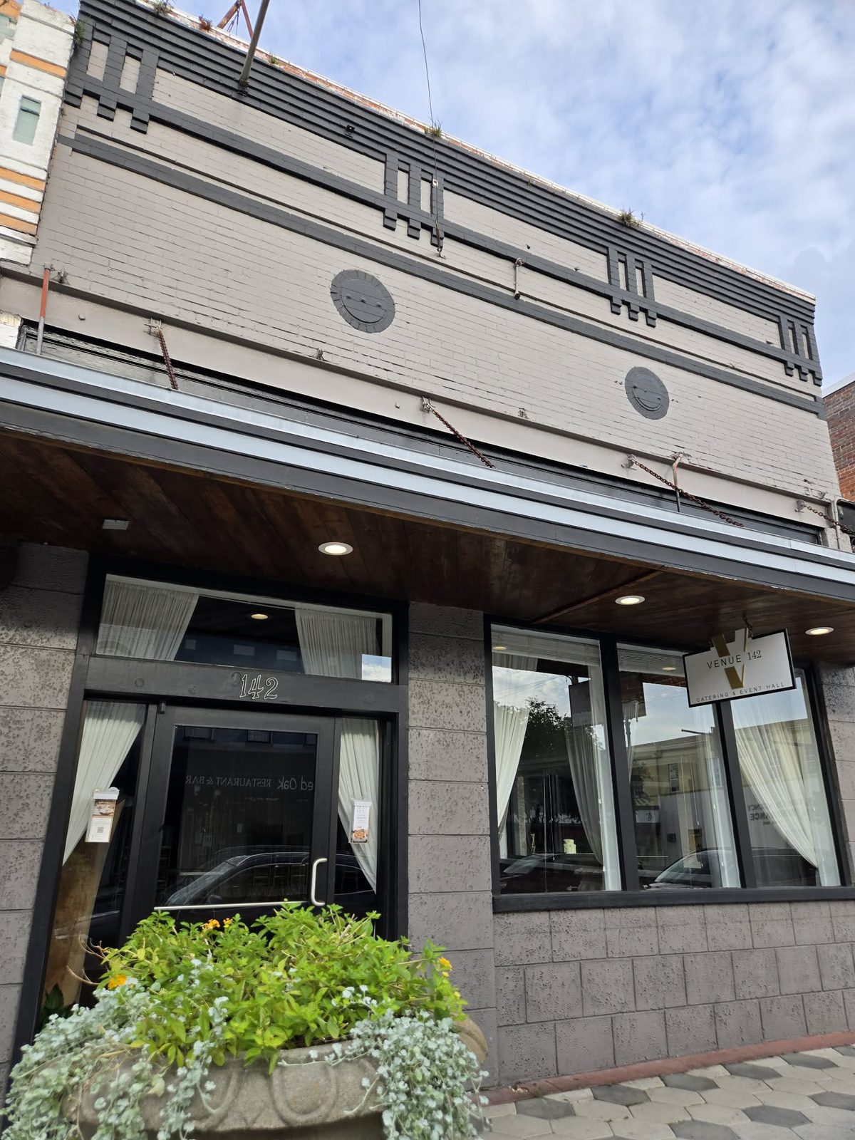 Gray Art Deco storefront with a hanging Venue 142 Catering and Event Hall sign in downtown DeLand.