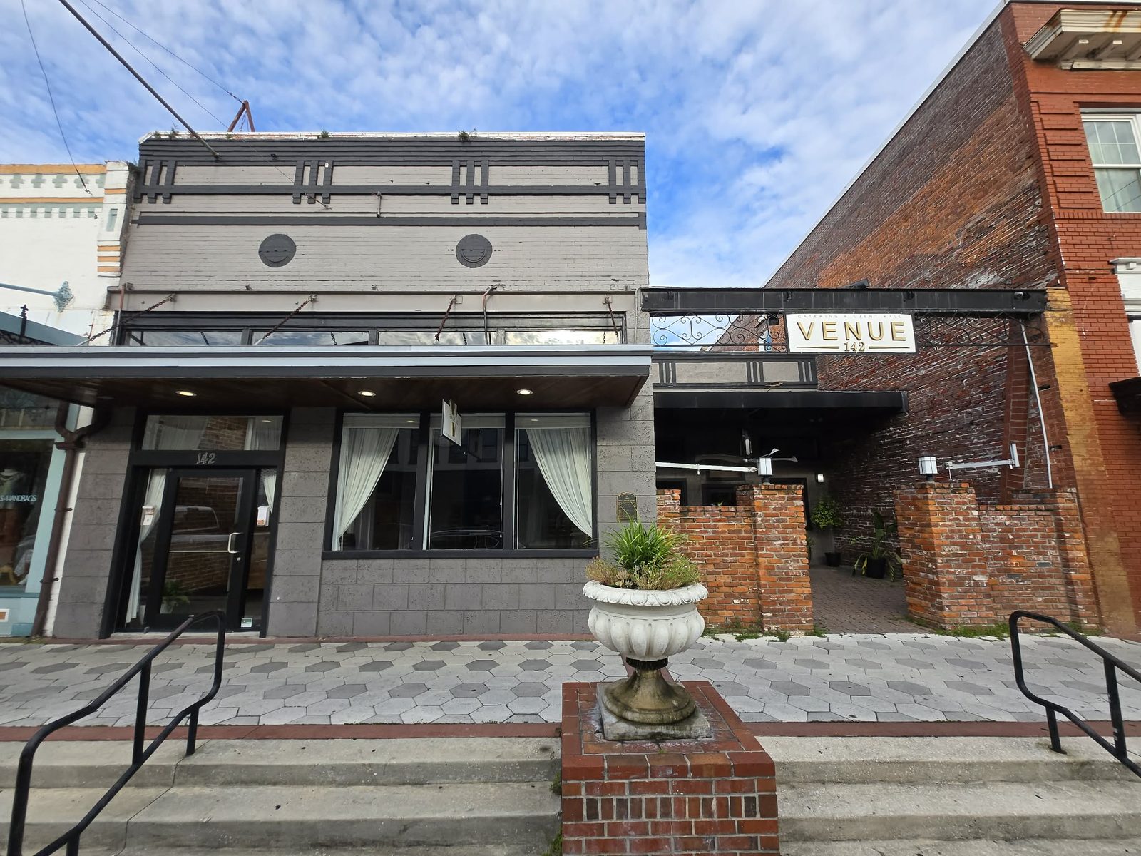 Gray Art Deco Venue 142 event hall with a hanging sign and a brick courtyard entry in downtown DeLand.