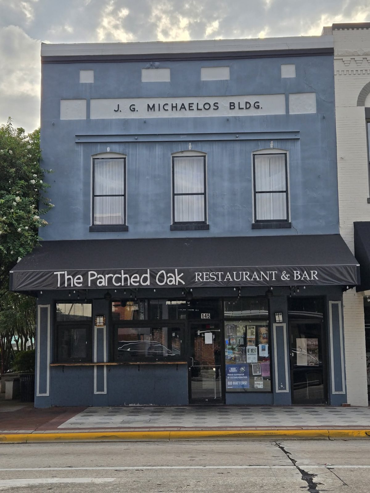 Blue-gray building with a black awning reading The Parched Oak Restaurant and Bar in downtown DeLand.