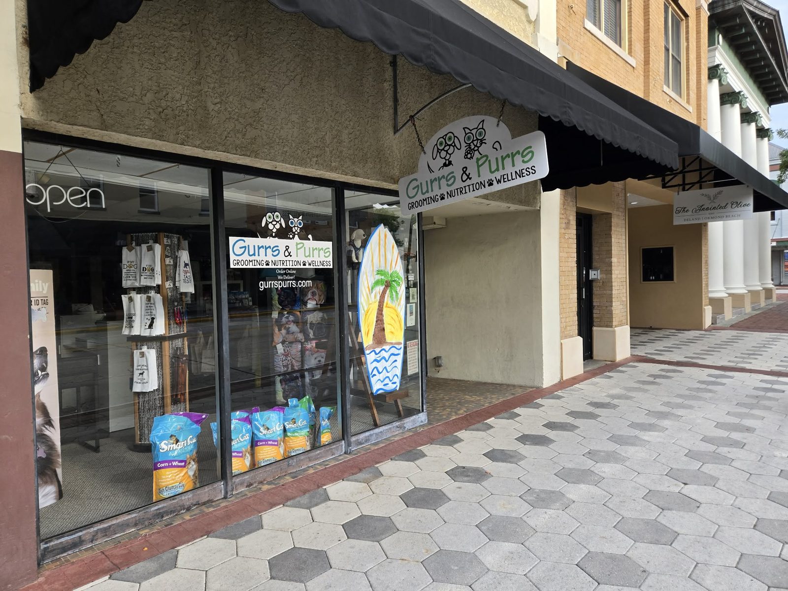 Angled storefront of Gurrs and Purrs pet shop with a hanging logo sign in downtown DeLand.