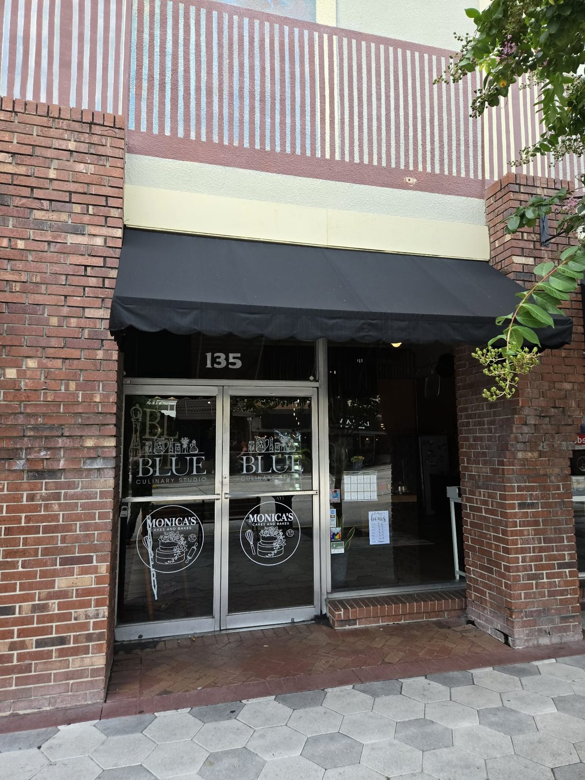 Brick storefront with a black awning and glass doors etched Blue Culinary Studio in downtown DeLand.