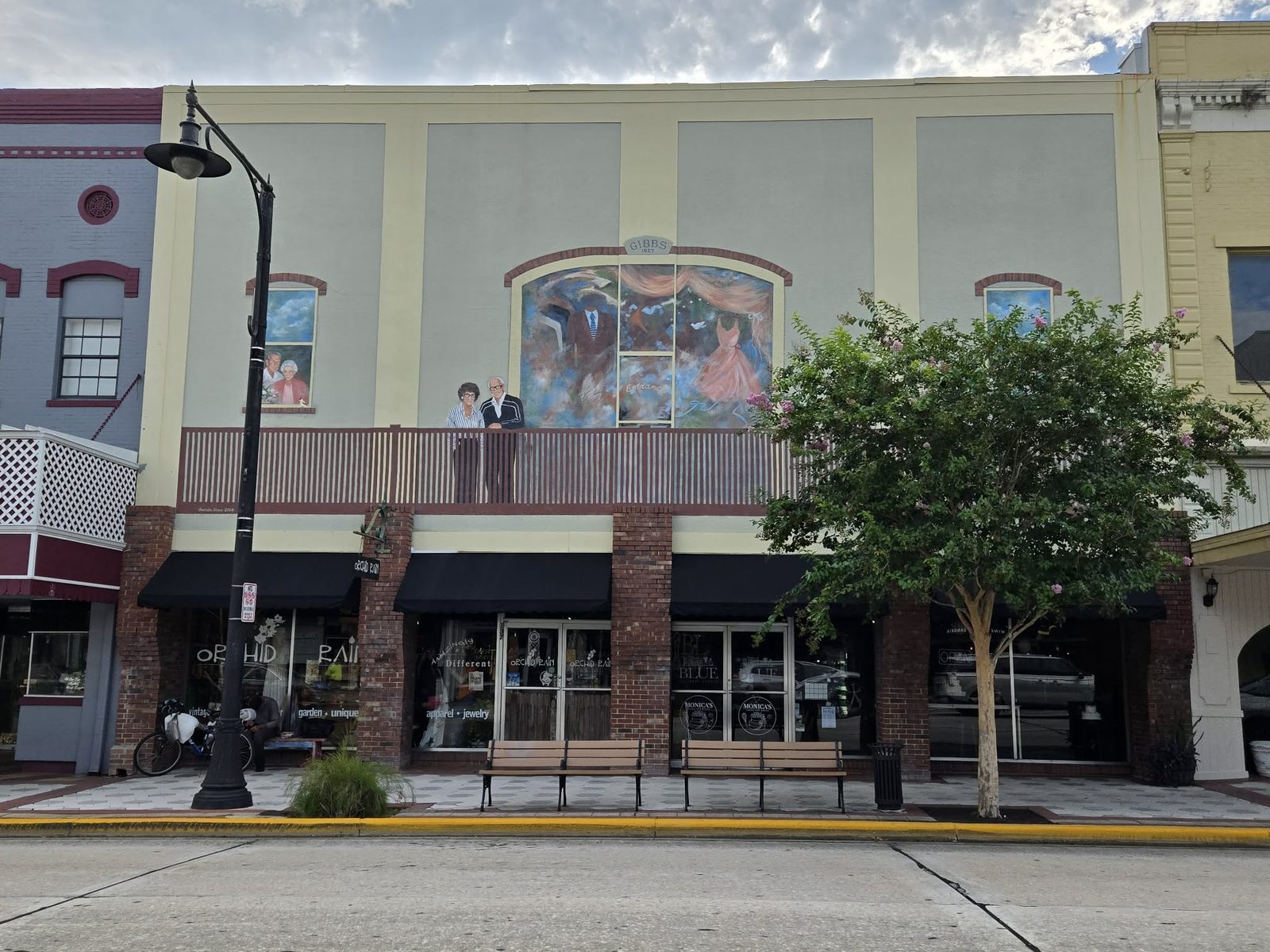 Trompe-l'oeil mural of an elderly couple at a balcony beside a clothing-store window, marked Gibbs 1937, in downtown DeLand.