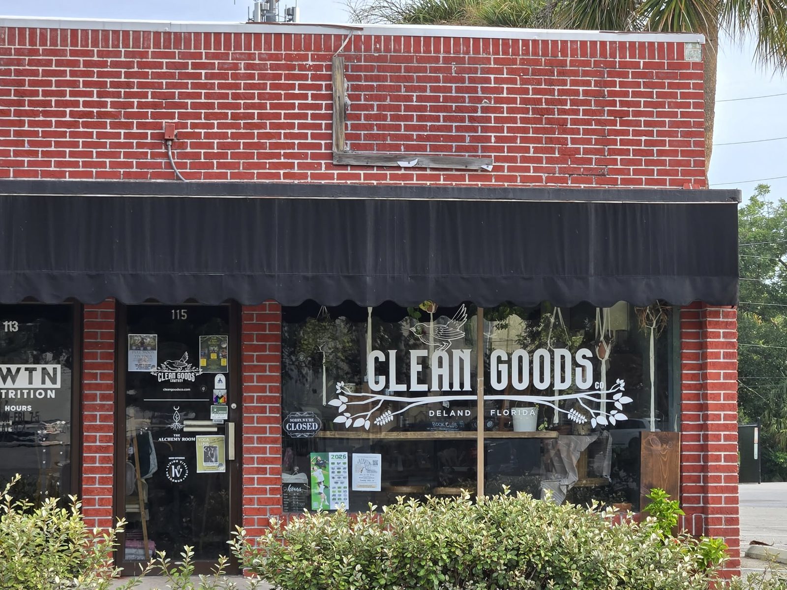 Brick storefront with Clean Goods Co painted on the window under a black awning in downtown DeLand.